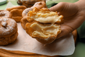 Woman holding delicious profiterole filled with cream above green table, closeup