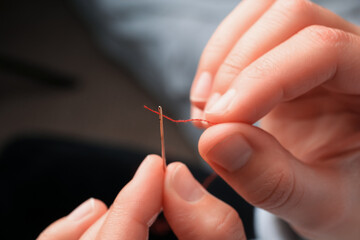 Woman threading sewing needle on blurred background, closeup