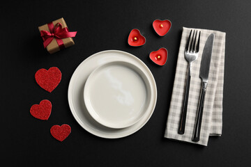 Beautiful table setting with burning candles and decorative hearts on black table for romantic dinner, flat lay