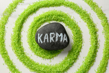 Stone with word Karma and circle made of light green sea salt on white marble table, top view