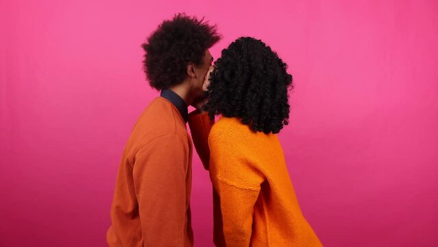 Close-up shot of male and female on a romantic date indoors. Portrait of a woman kissing her boyfriend with pink isolated background behind. High quality 4k footage