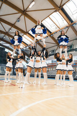 Cheerelading team divided into three groups, each doing an extension stunt. Vertical photo. Sport...