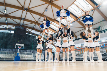 Low angle shot. Three groups of cheerleaders holding their teammates in the air. Extension stunt....