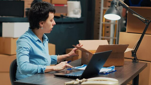 Business owner analyzing boxes with merchandise to ship order to clients, working on products distribution. Woman planning quality control and taking notes on laptop, supply chain management.