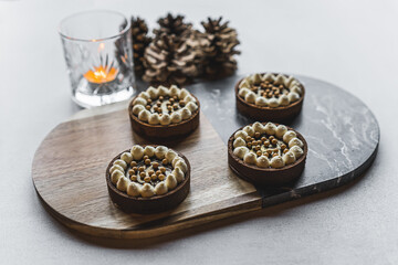 Wooden and marble platter with four mini chocolate sweet tarts next to candle and pinecone decoration. Winter holiday desserts. Horizontal shot. High quality photo