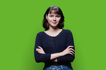 Fototapeta premium Young smiling female with crossed arms on green background
