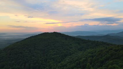 Aerial view of green pine forest with dark spruce trees covering mountain hills at sunset. Nothern woodland scenery from above
