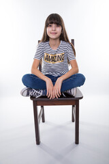 smiling teen girl sit with crossed legs on chair rest and chill for a moment at isolated studio with striped shirt and 'amazing' text on it