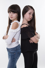 two female siblings stand back to back with arms crossed arms isolated on white in black and white...