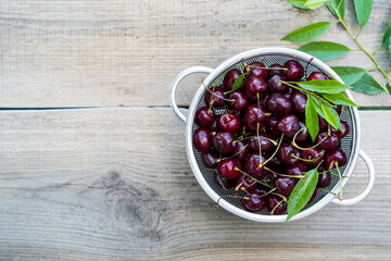 cherry berries on a wooden table in a colander, summer food, top view, place for text