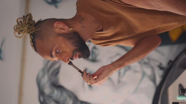 Black brazilian gay applaying make up eyeshadow looking mirror view from behind. Non binary androgynous guy. LGBT concept Close up face Vertical video for reels social media
