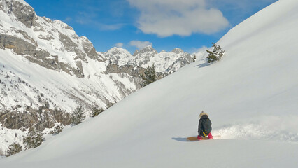 Lady on a snowboard riding fresh powder snow and making a turn on snowy slope