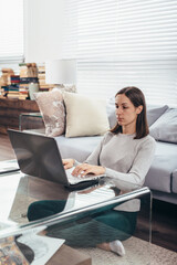 Woman sitting on floor and leaning to sofa using laptop.