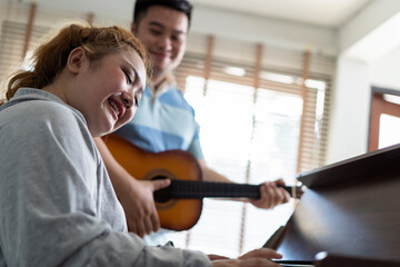 Young Asian chubby couple singing and playing acoustic guitar and piano together. Man and woman enjoying musical instrument. People in a band practicing in the house