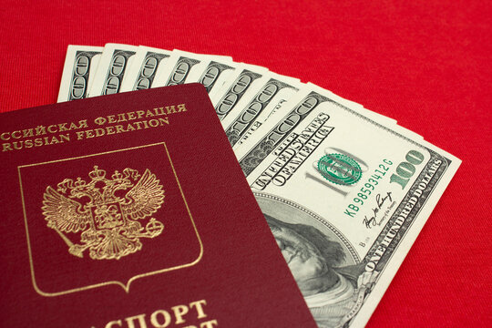 Photo of biometric Russian passport and green paper American bill on red textile background. 100 USD. One hundred dollars. USA cash. Money. Concept of immigration from Russia to America. Travel. Trip