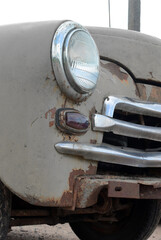 Vertical photo. Vintage dirty white car. Round headlight of retro car. Concept of obsolescence,...
