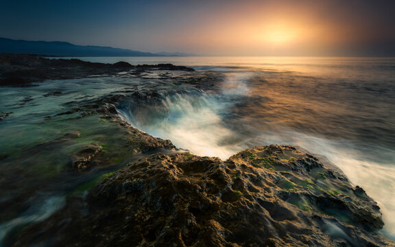 Scenic view of waves splashing on rock formations against sky during sunset