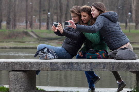 Teen girls relax on bench, taking selfie