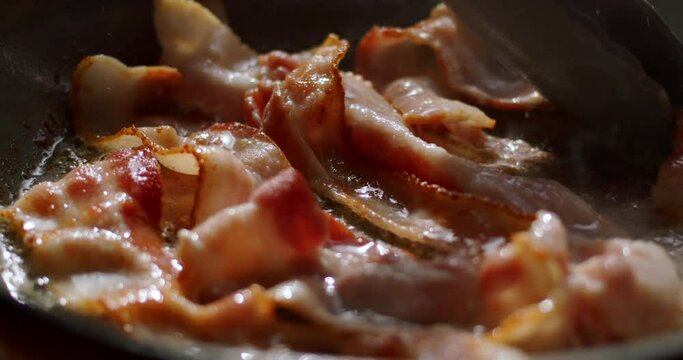 Tracking Close-up of hot sizzling bacon frying in a pan.  4K ProRes 422 HQ DCI 4096 x 2160. Shot on the Blackmagic Cinema Camera 6K Pro on a slider, with rack focus and natural morning light.