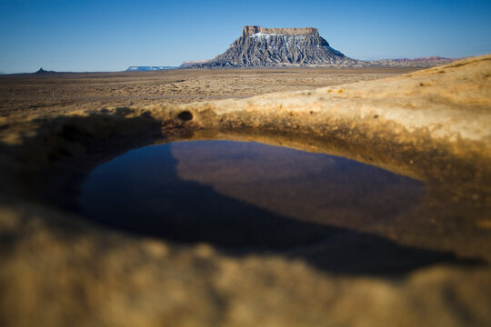 Factory Butte as seen from a pool of water formed in a natural depression in rock, near Hanksville, Utah.