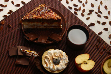 A sweet still life of cakes, milk chocolate, a cup of tea, an apple, an amber pendant, and beech seeds.