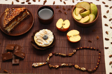 Obraz na płótnie Canvas A sweet still life of cakes, milk chocolate, a cup of tea, an apple, an amber pendant, and beech seeds.