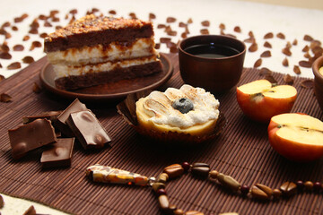 A sweet still life of cakes, milk chocolate, a cup of tea, an apple, an amber pendant, and beech seeds.