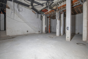 Raw underground premises with cement floors and grooves for pipes and wiring hanging from the...