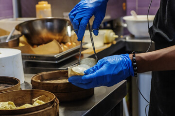 An Asian chef with gloved hands preparing dumplings for home delivery