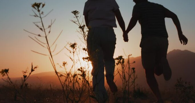 Silhouette of couple running in a mountain field at sunset, holding hands, young and romantic family enjoying. Back view slow motion