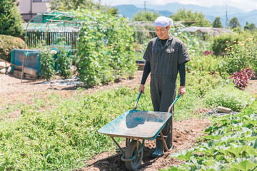 キャリーカートを持って畑を歩く農家のアジア人男性（農業・田舎暮らし）