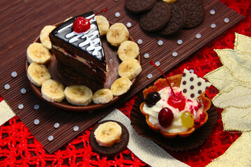 Sweet still life of cakes, cocoa cookies, yogurt cups, sliced bananas, red coral beads, bracelet with Ukrainian ornament, and beads on a red napkin.