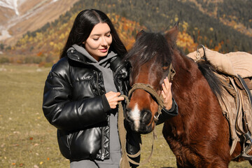 Young woman stroking horse in mountains on sunny day. Beautiful pet