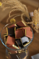 Glass vase with chocolate candies on wooden table, closeup