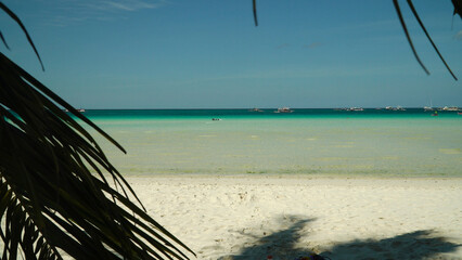 Tourists on a sandy beach and blue sea through palm branches. Summer and travel vacation concept. Boracay, Philippines