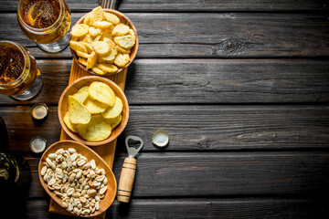 Beer and various kinds of snacks in the bowls on the cutting Board.