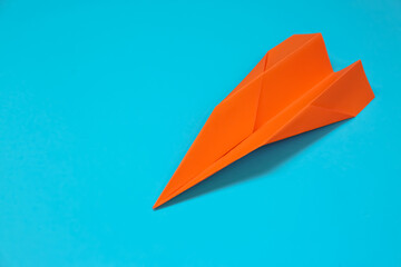 Orange paper plane on light blue background, space for text