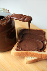 Tasty toast with chocolate paste, knife and jar on wooden board, closeup