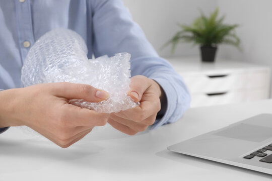 Woman Popping Bubble Wrap At Table In Office, Closeup. Stress Relief