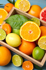 Different ripe citrus fruits with green leaves on light blue wooden table, flat lay