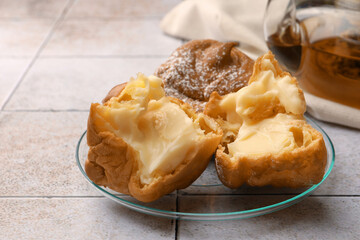 Delicious profiteroles filled with cream on white tiled table, closeup