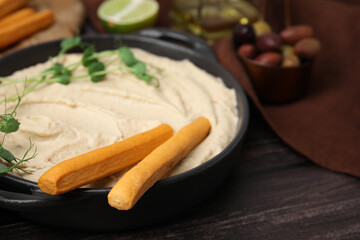Delicious hummus with grissini sticks and ingredients on wooden table, closeup