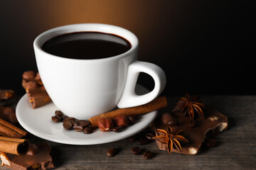 Cup of delicious hot chocolate, spices and coffee beans on wooden table