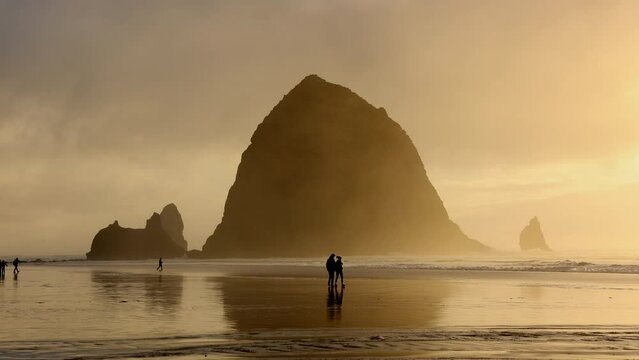 People enjoying beautiful sunset over Oregon coastline. Cinematic landscape of idyllic Cannon Beach with low tides crashing against the shore. High quality 4k footage