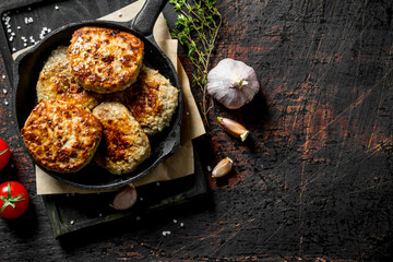 Cutlets in pan on paper with thyme,garlic and tomatoes.