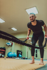 A fit athlete man doing intense battle rope exercise at crossfit gym.