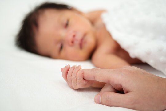newborn baby hand holding index finger of mother on bed