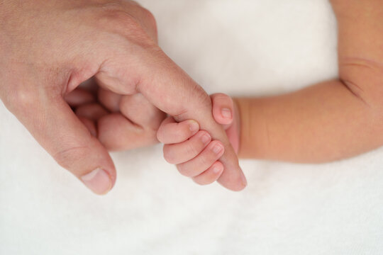 newborn baby hand holding index finger of mother on bed
