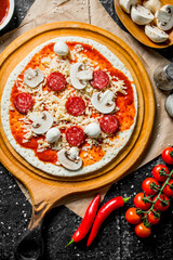 Raw pizza with sausages, chili and mushrooms.