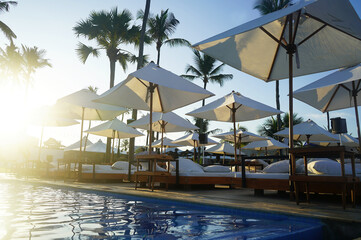Luxury umbrellas and chairs around outdoor swimming pool with beach view. Luxurious vacation and holiday concept.